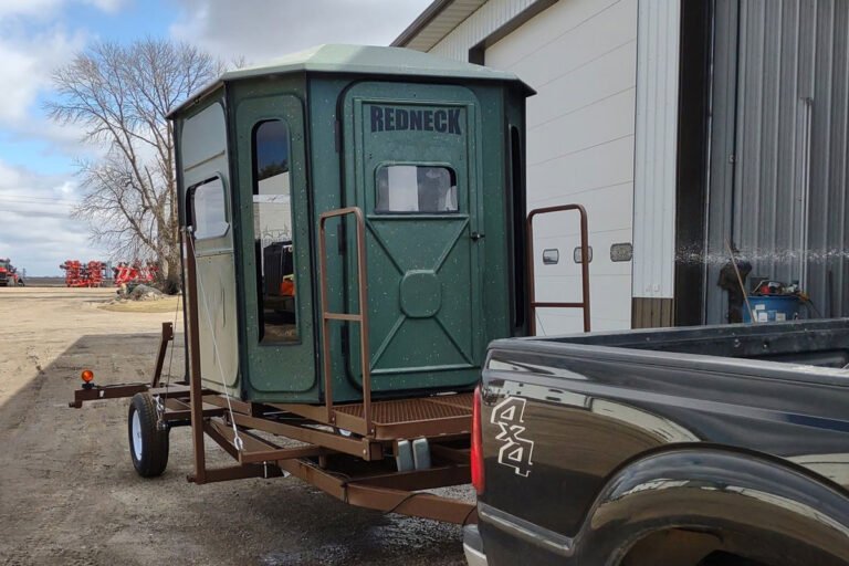 Pickup truck towing a mobile hunting blind on a trailer.